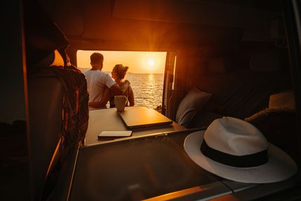 Un uomo e una donna sono seduti sul retro di un furgone e guardano l'oceano al tramonto.