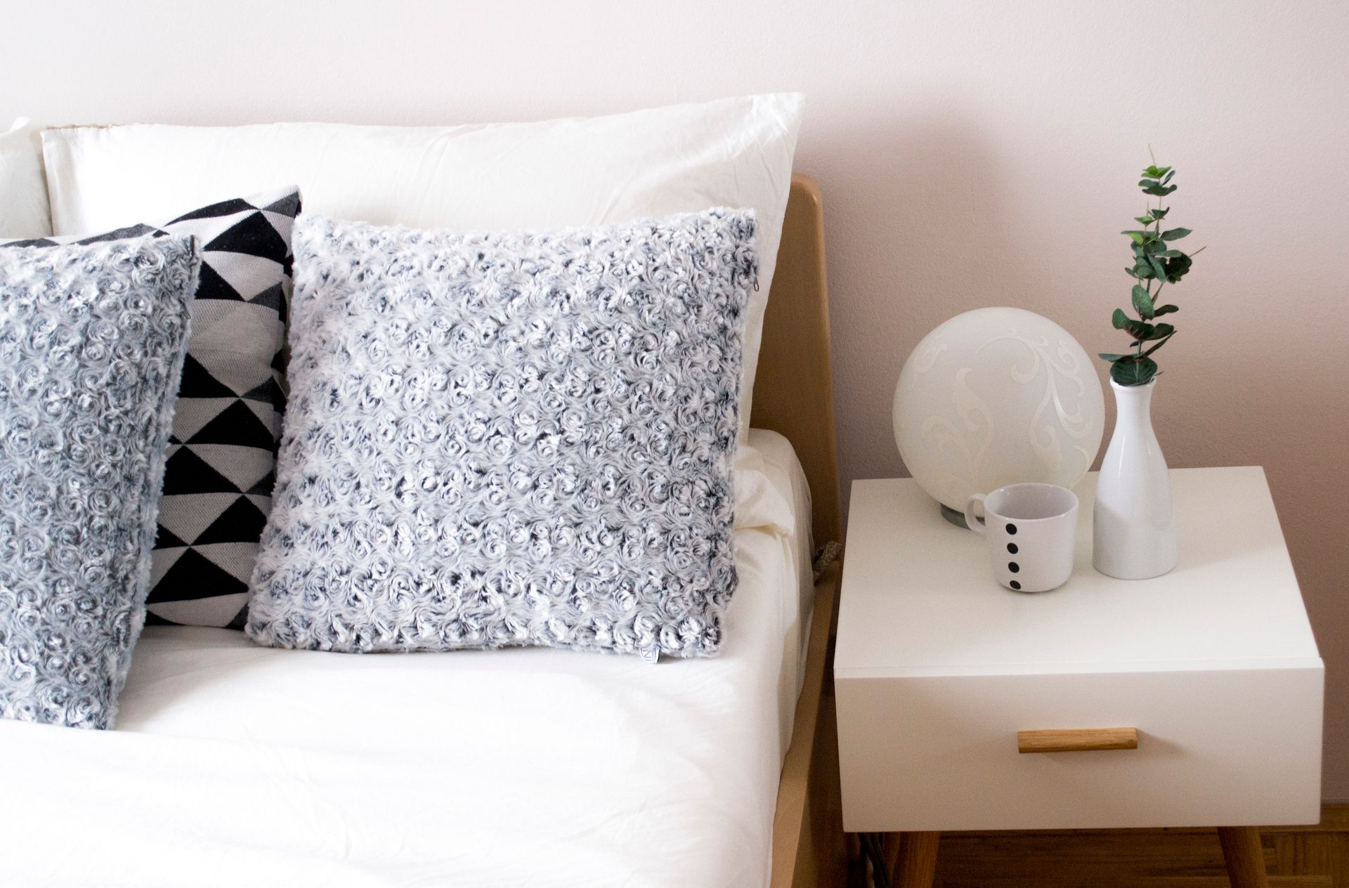 A bed with pillows and a nightstand with a vase of flowers on it.