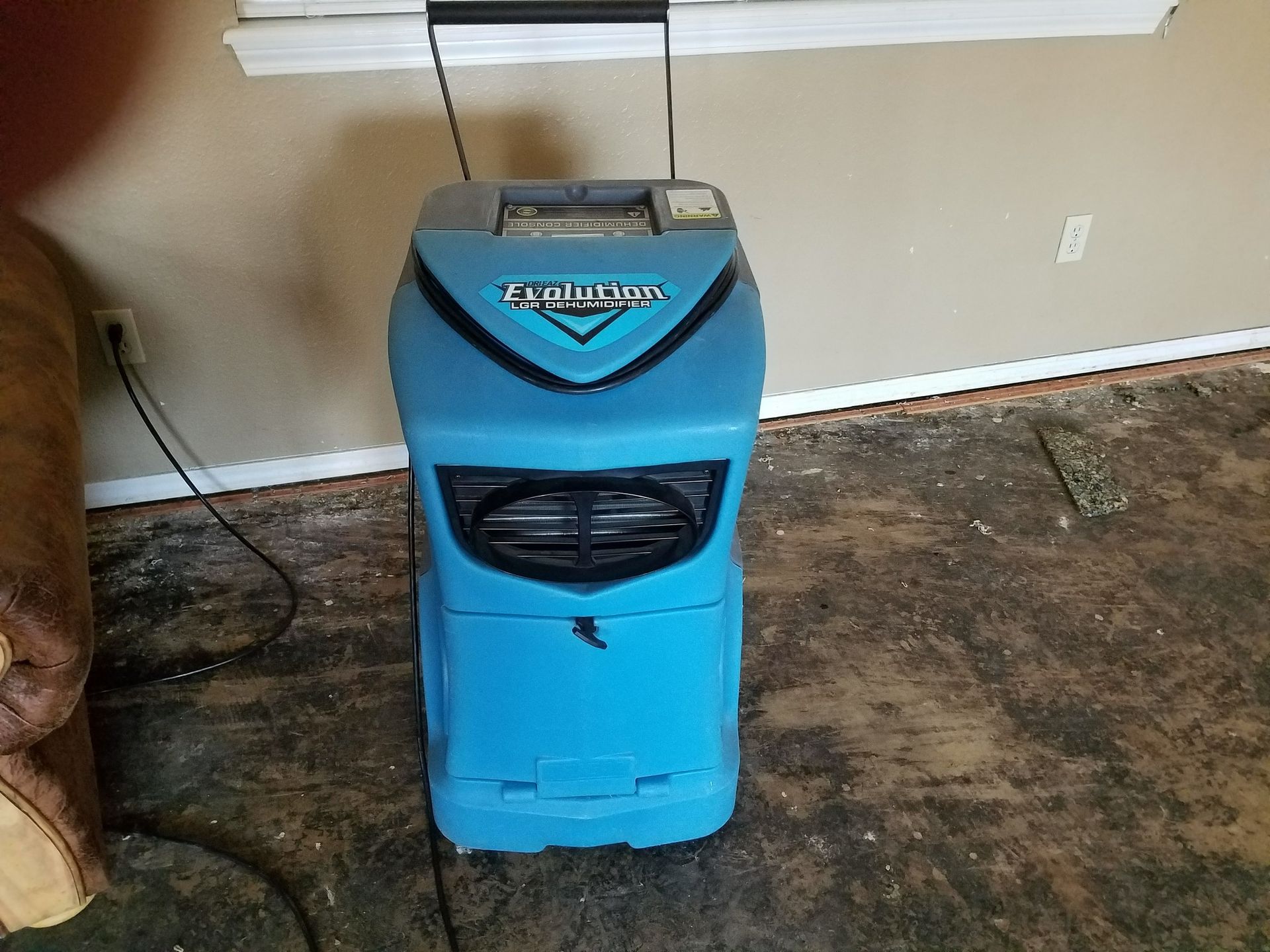 Blue dehumidifier in room with damaged flooring, near a window.