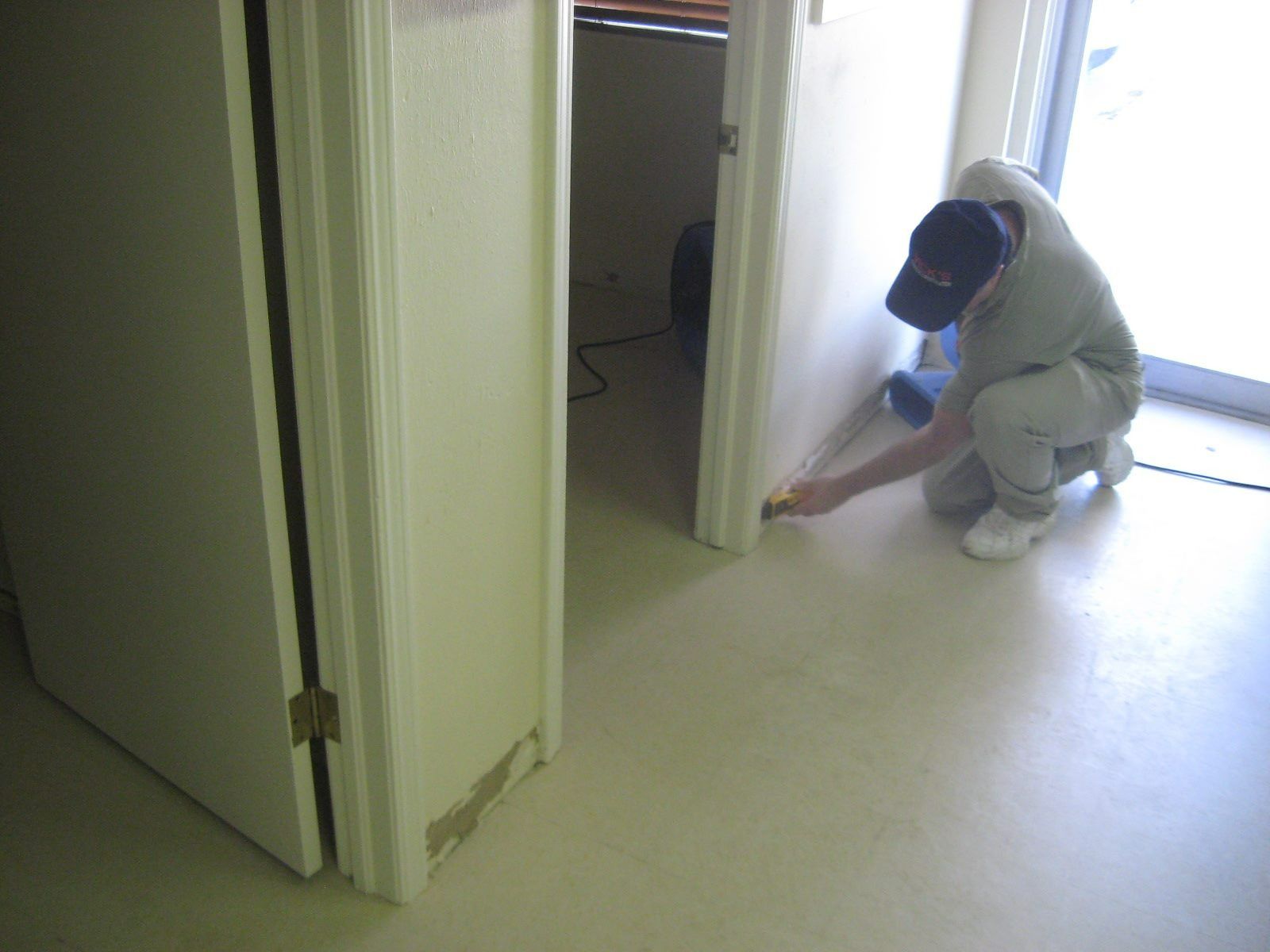 Person painting a room, kneeling near a door frame. White walls, beige floor.