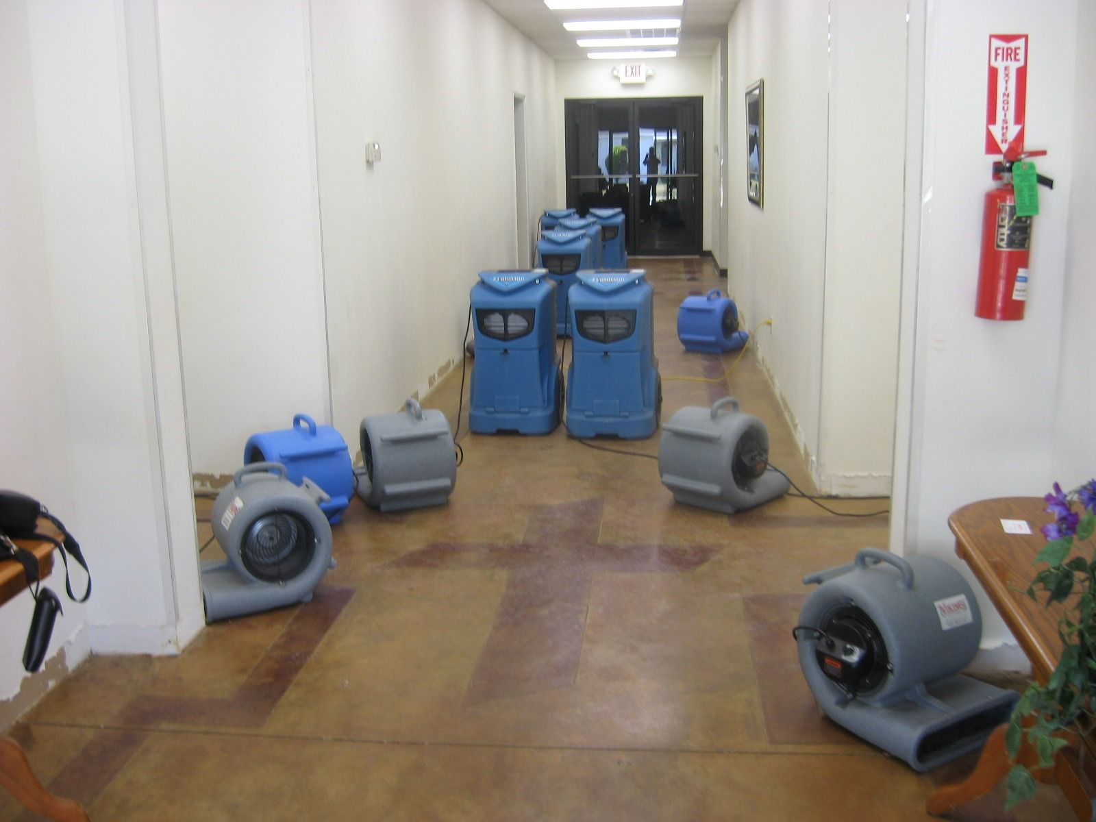 Hallway with several blue and gray air movers, likely for drying after water damage.