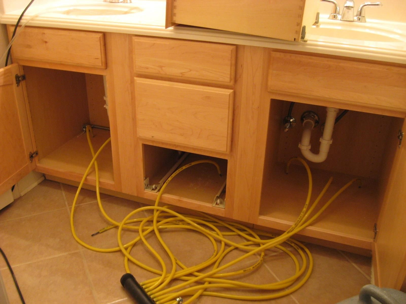 Open bathroom vanity with exposed plumbing and yellow extension cords.