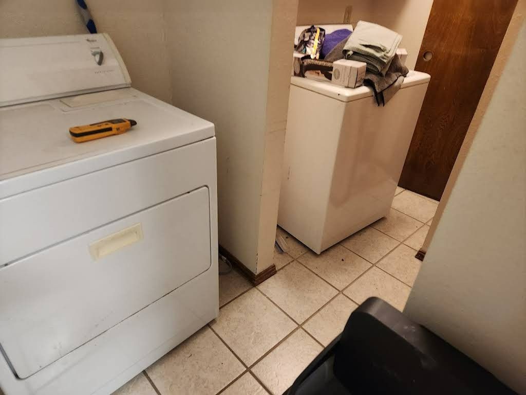 Laundry room with white washer and dryer, small tools, and tile floor.