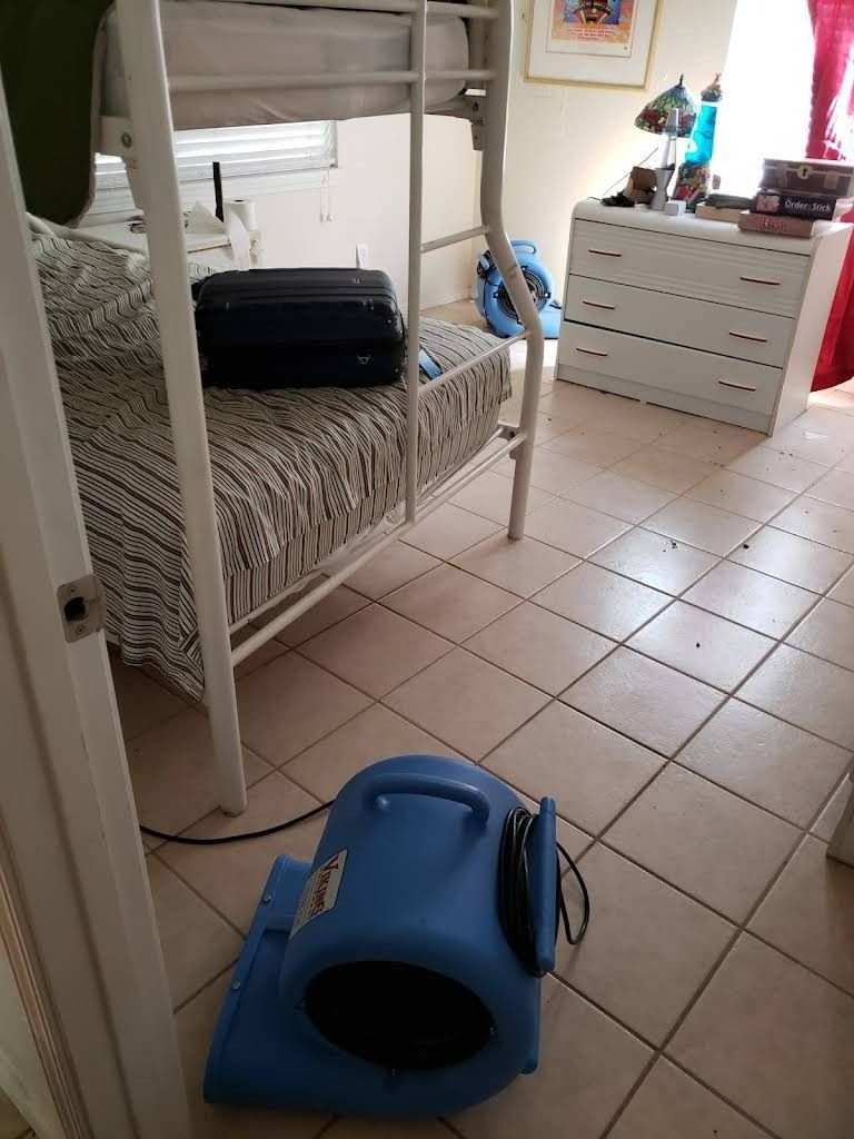 Blue fan drying a room with bunk beds, suitcase, and white dresser.