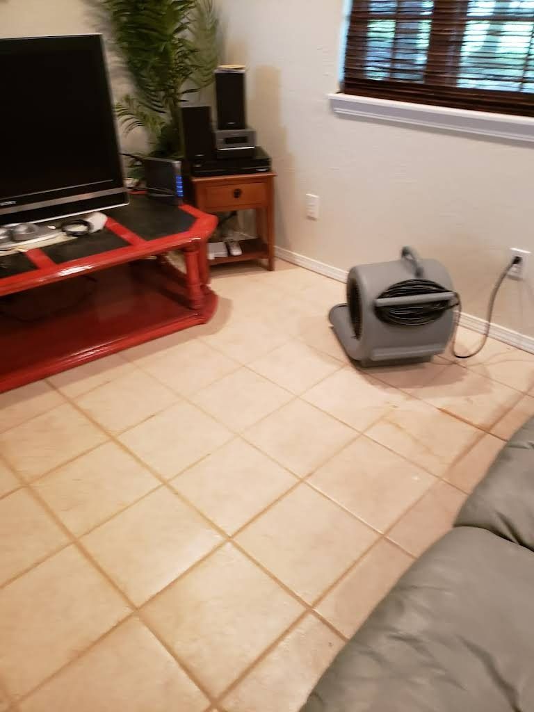 A gray air mover sits on tile floor in a room with a TV, table, and window.