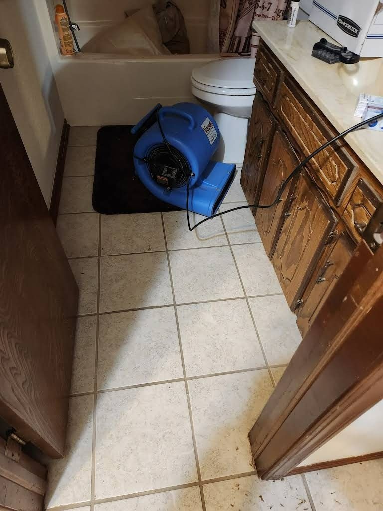 Blue air blower in a bathroom with beige tile flooring and wooden cabinets.