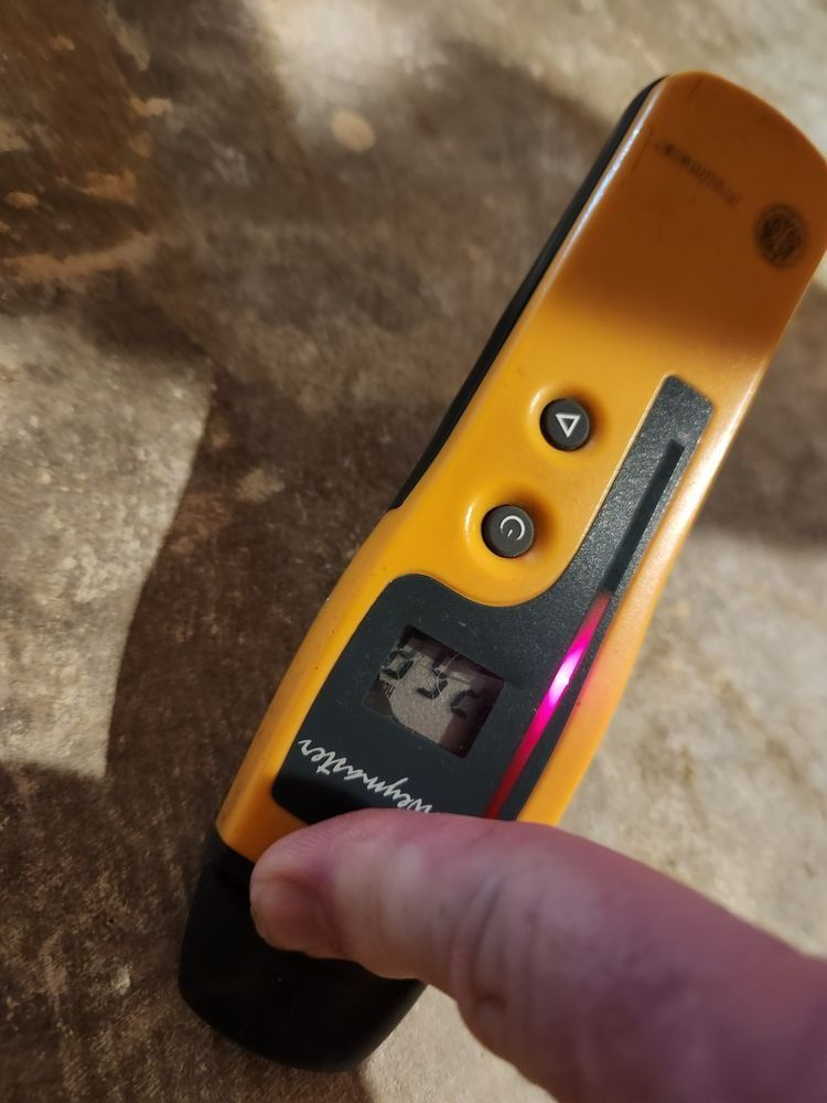 Yellow and black stud finder being held by a person, display showing 3.56.