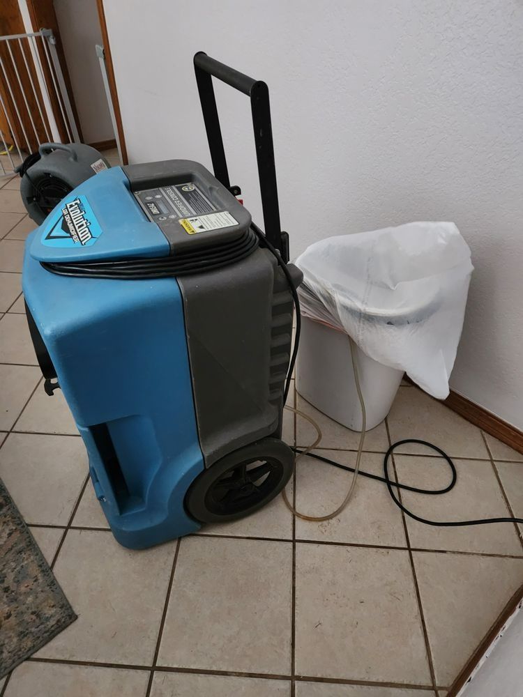 Blue and gray dehumidifier with a trash bag attachment on a tiled floor.