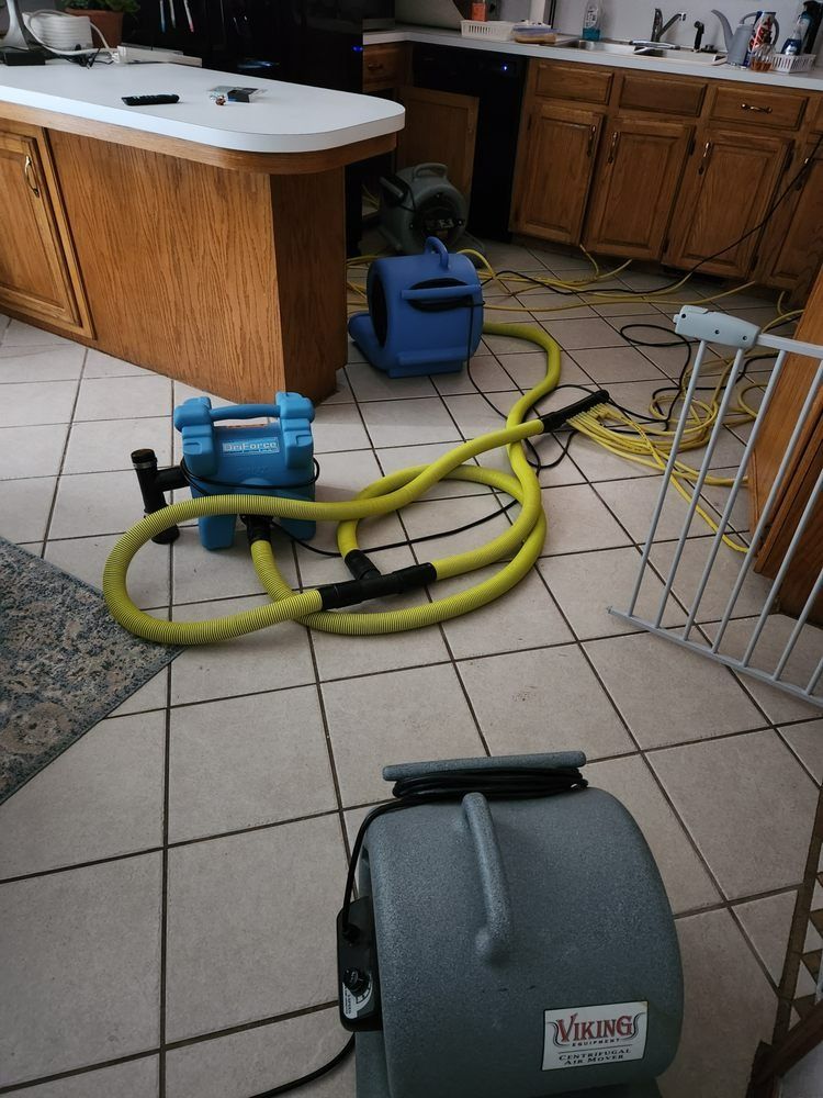 Kitchen with water damage equipment: fans, hoses, and pumps on tile floor.