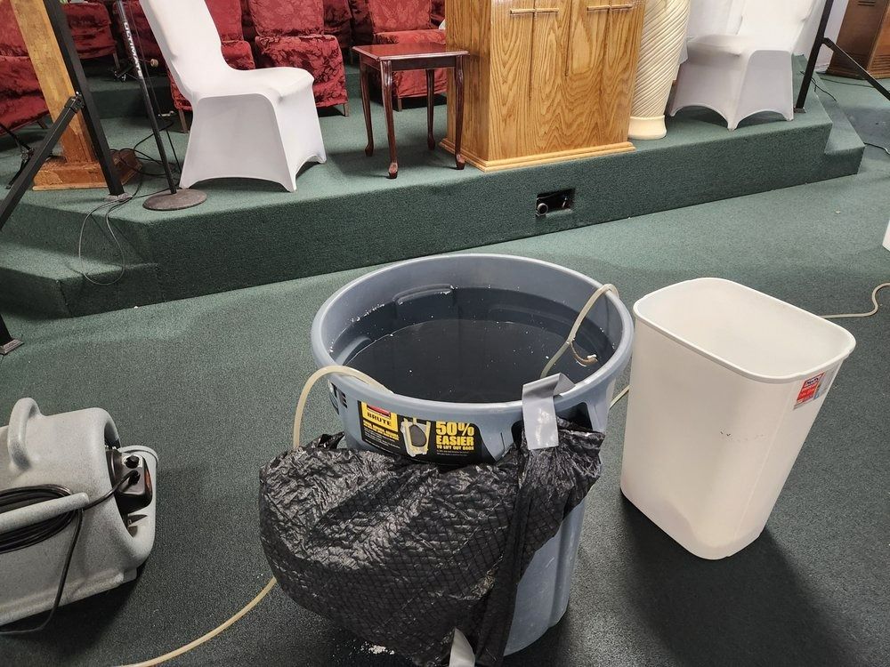 A large gray bucket of water with a pump is on a green carpeted stage. A blower fan is to the left.