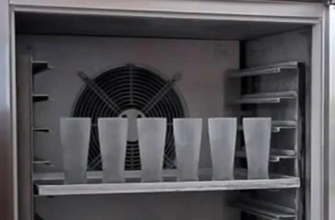 A refrigerator filled with empty cups and a fan.