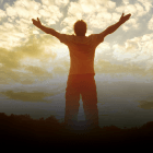 A man is standing with his arms outstretched in front of a cloudy sky.