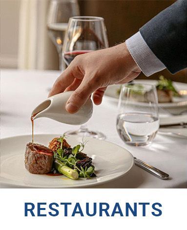 A person is pouring sauce on a plate of food at a restaurant.