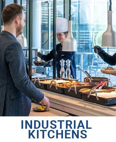 A man in a suit is standing in front of a buffet line in an industrial kitchen.