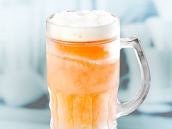 A glass of beer with foam on top is sitting on a table.