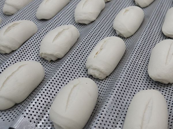 A bunch of white bread rolls are sitting on a perforated tray.