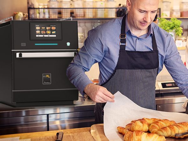 A man in an apron is preparing croissants in a kitchen.