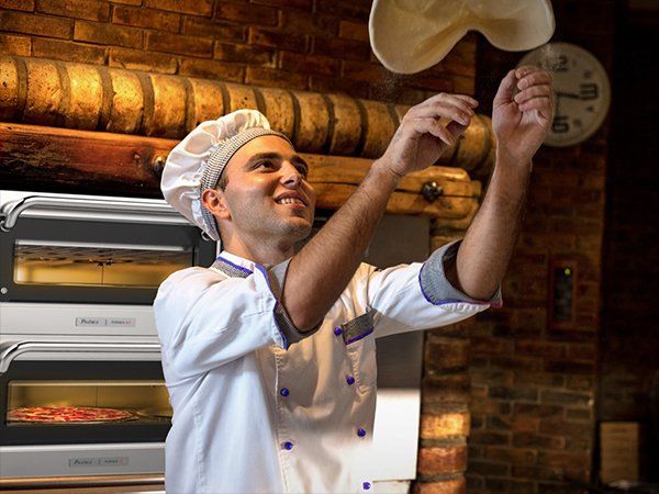 A man in a chef 's uniform is throwing pizza dough in the air.