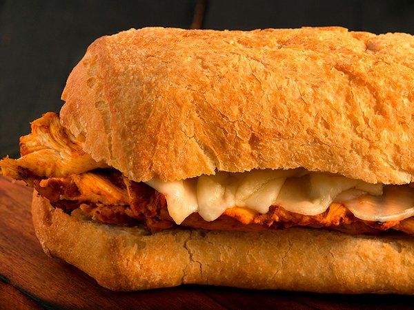 A close up of a chicken sandwich on a bun on a wooden table.