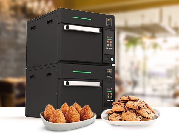 Two black ovens are stacked on top of each other next to a plate of cookies.