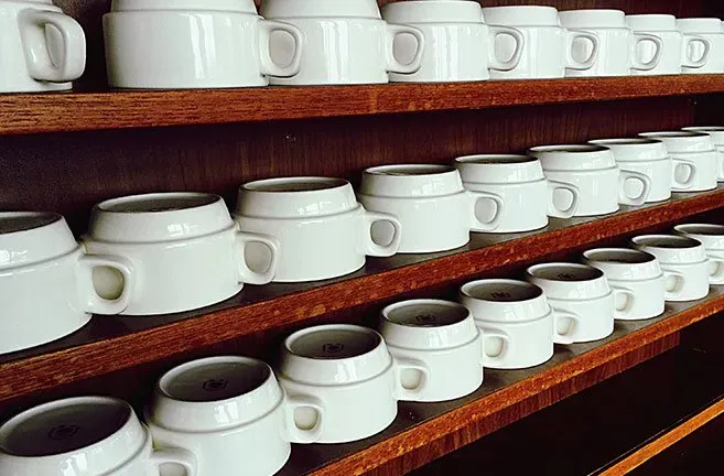 A row of white coffee cups on a wooden shelf