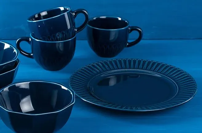 A set of blue plates , bowls , and cups on a blue table.