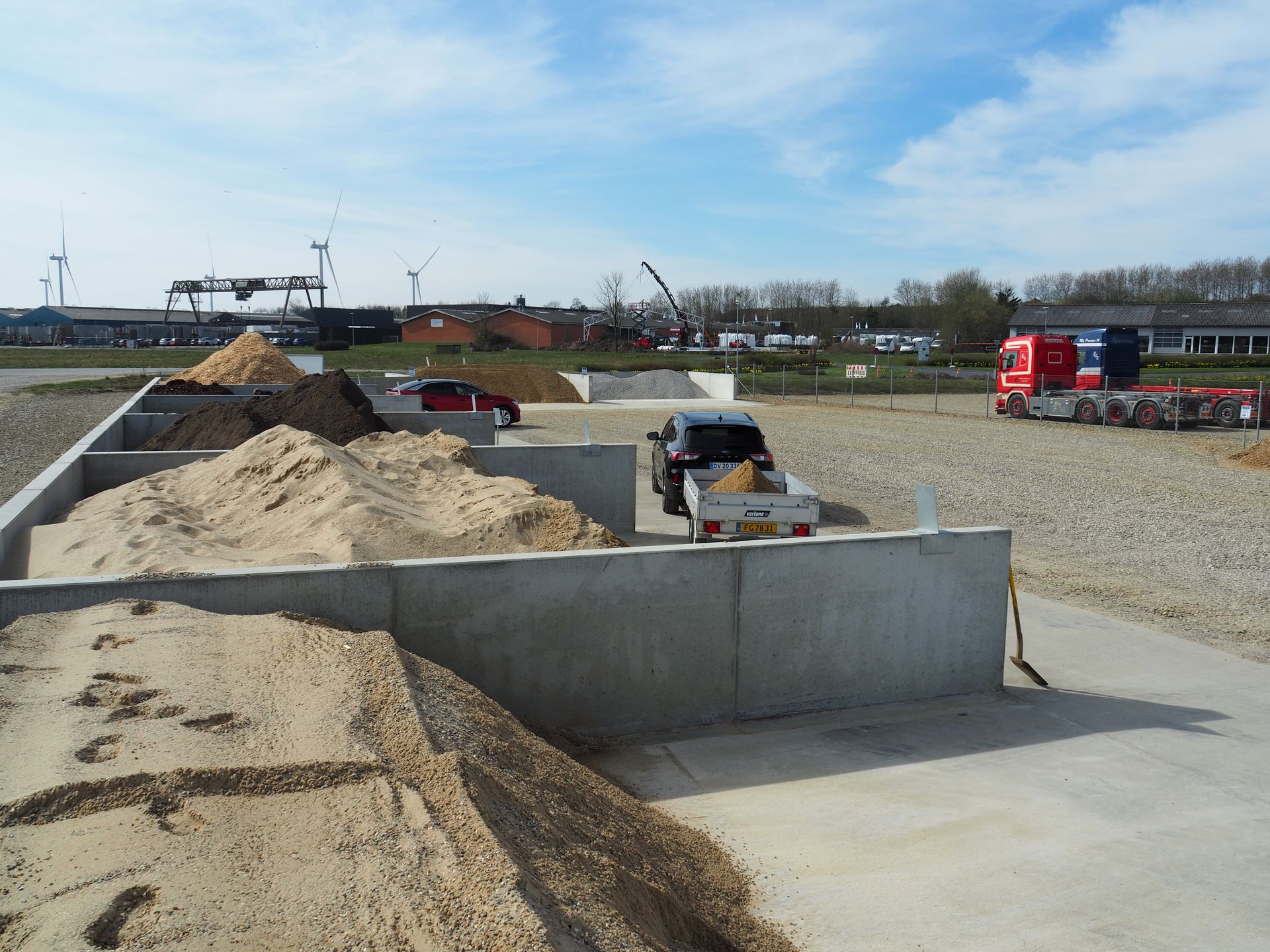 Opbevaringsanlæg til sand og træflis med køretøjer og entreprenørudstyr.