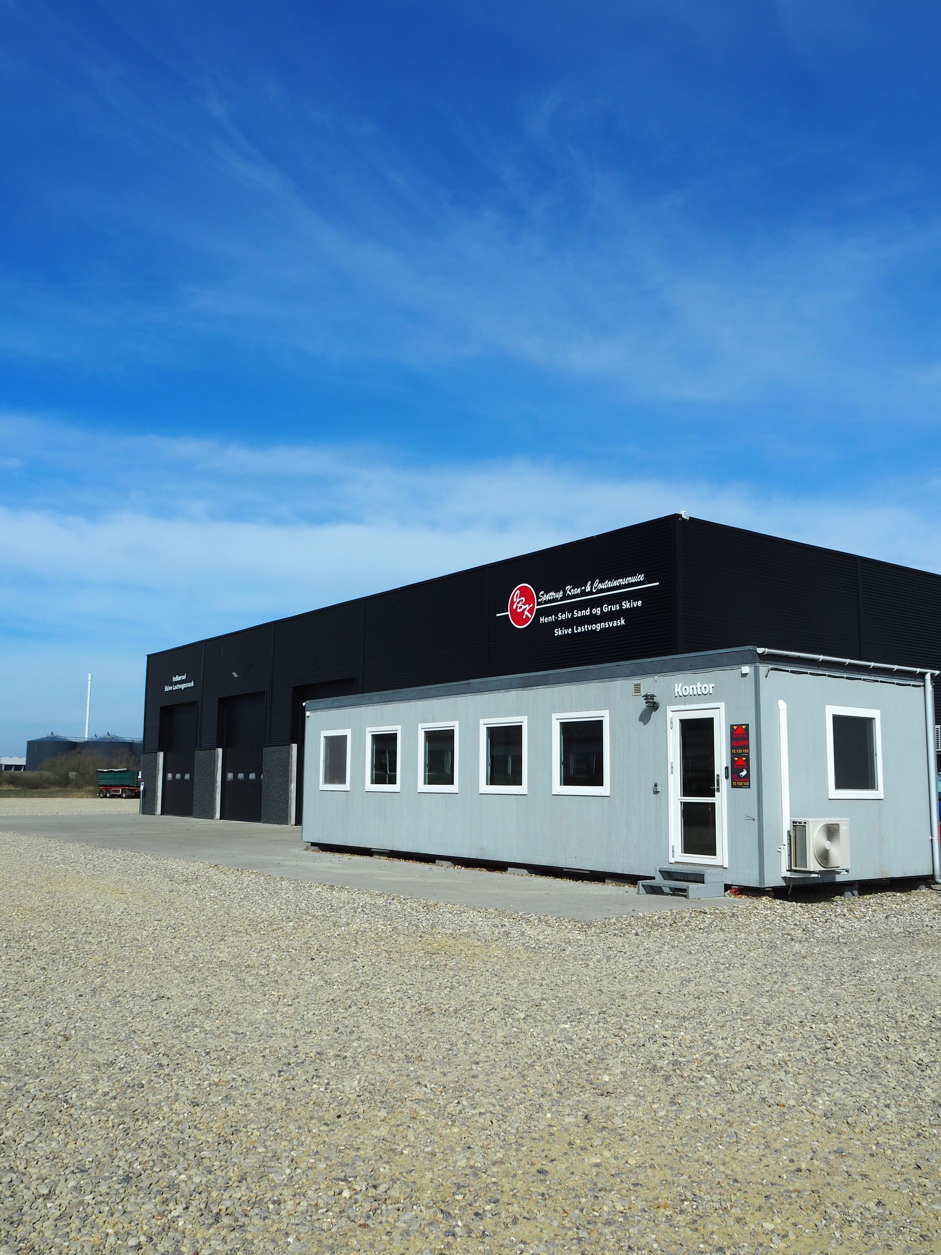 Rød Volvo lastbil og blå/rød varevogn parkeret på en grusplads med grusbunker i baggrunden.