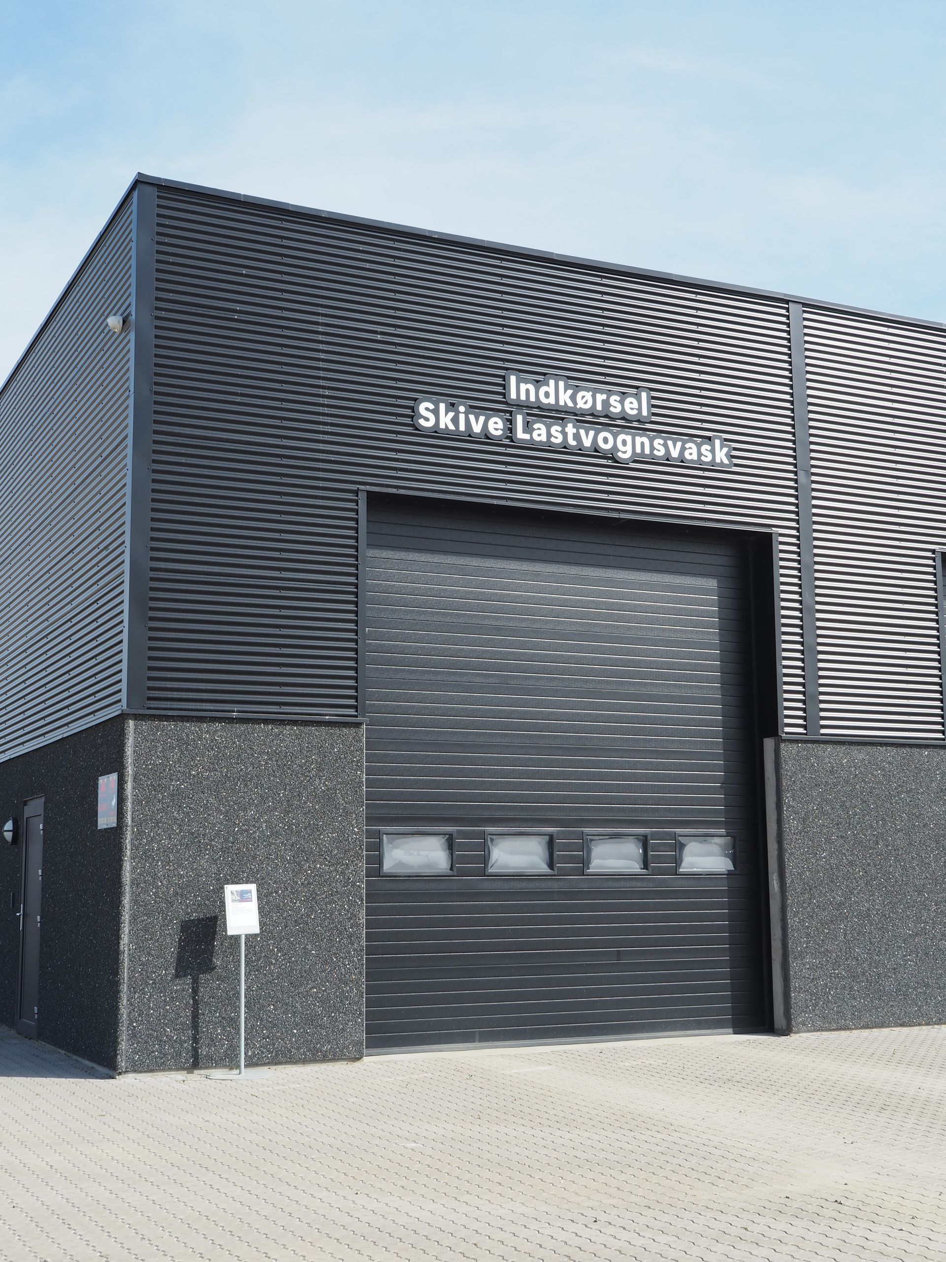Black industrial building with a large garage door; the sign says 