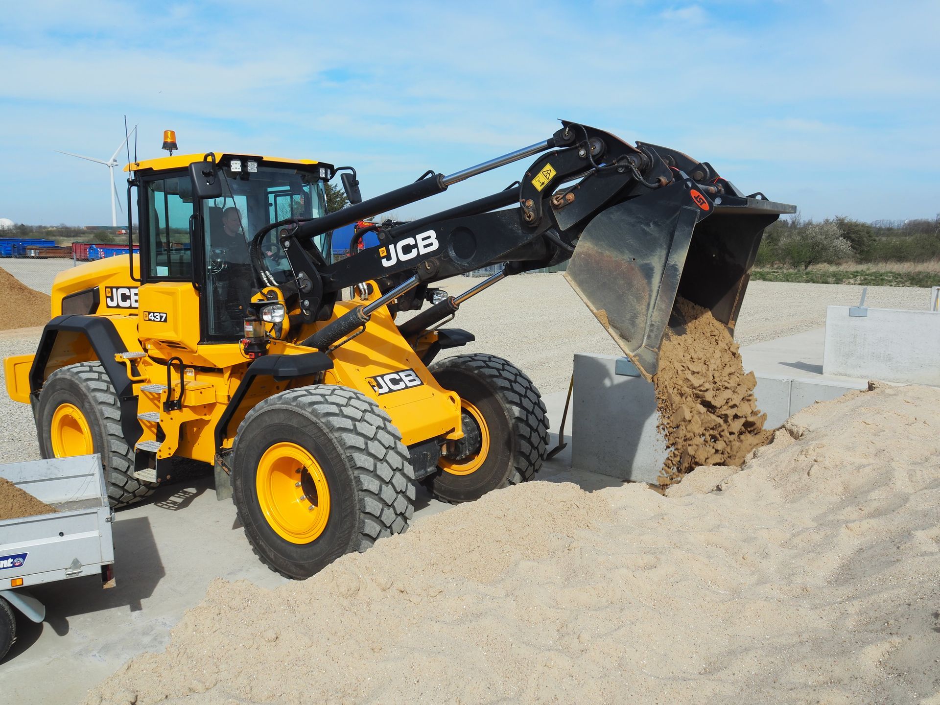 Gul JCB-læsser tømmer sand på betonblokke.