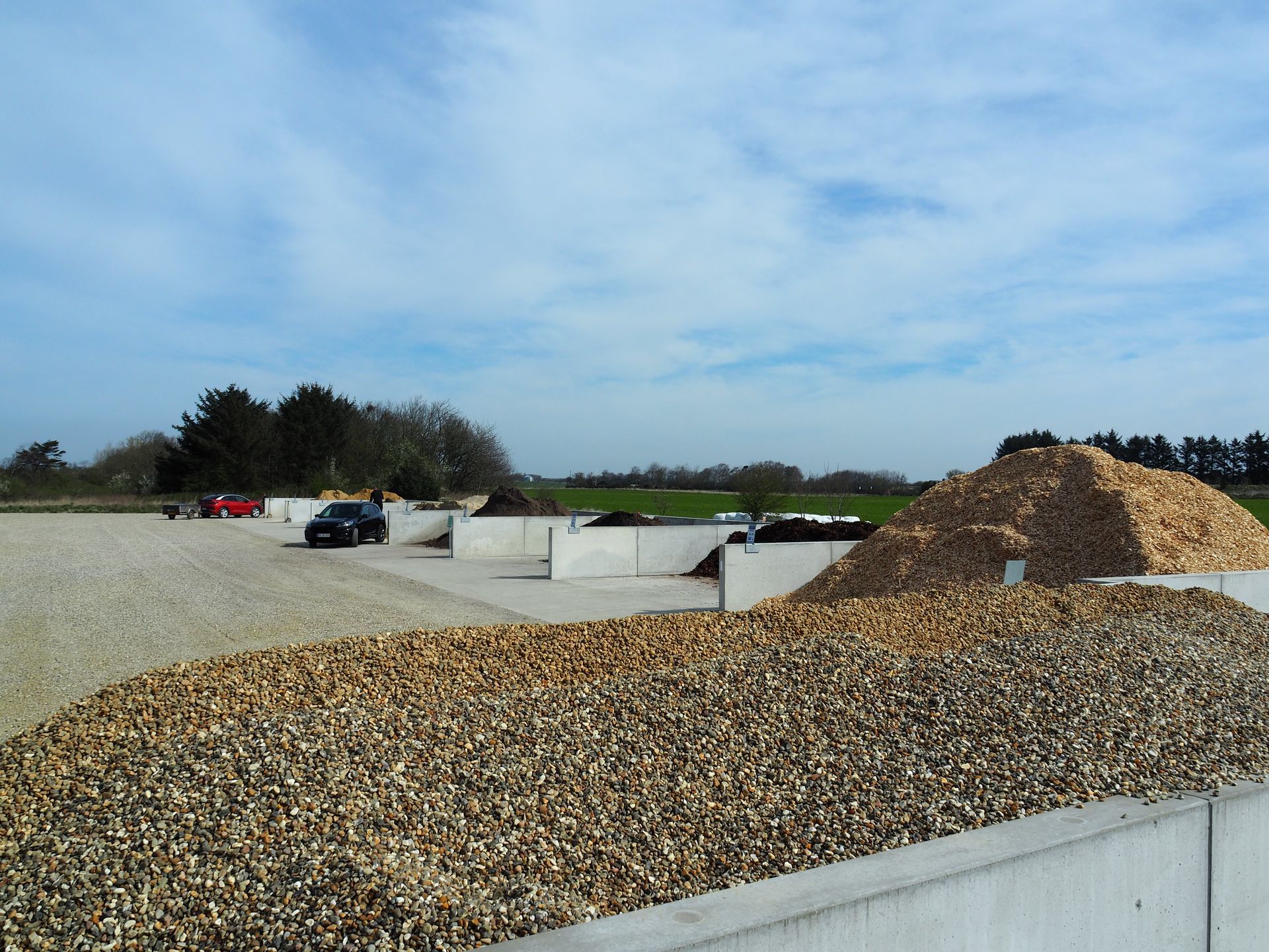 Opbevaringsområde til træflis med bunker af træflis og betonvægge under en overskyet himmel.