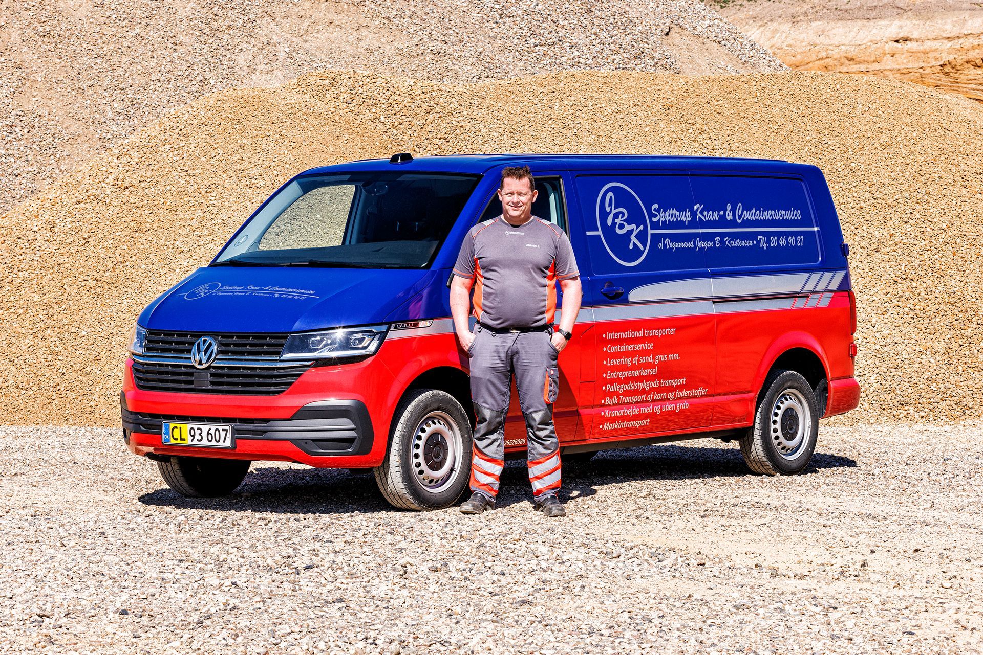 To røde og blå semitrailere parkeret udendørs på grus under en blå himmel.