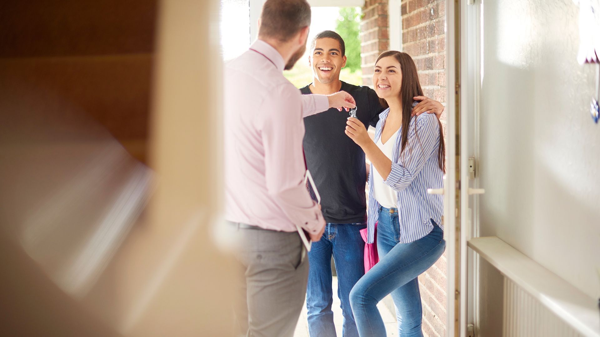 Real estate agent handing keys to a couple at a doorway; they are smiling.