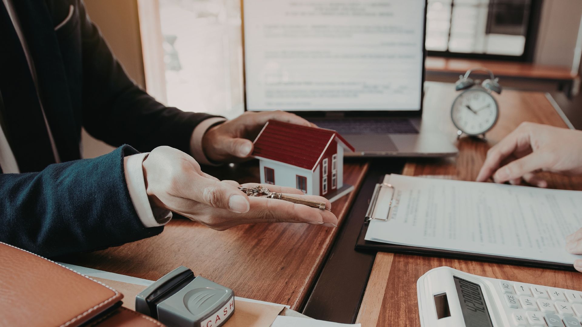 Hands with a model house and documents on a desk, discussing a real estate deal.