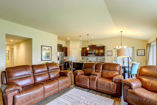 Cozy living room with brown leather furniture, open to a kitchen and dining area. Neutral wall paint and hardwood floors.