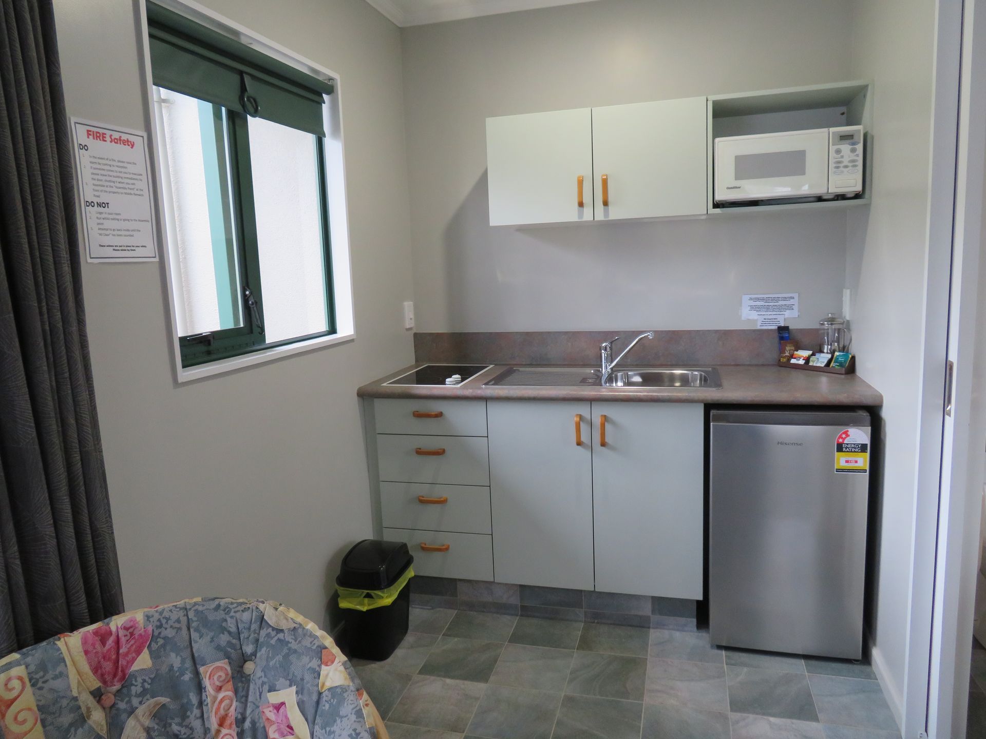 A small kitchenette featuring light grey cabinets, a sink, a microwave, and a compact stainless steel refrigerator.
