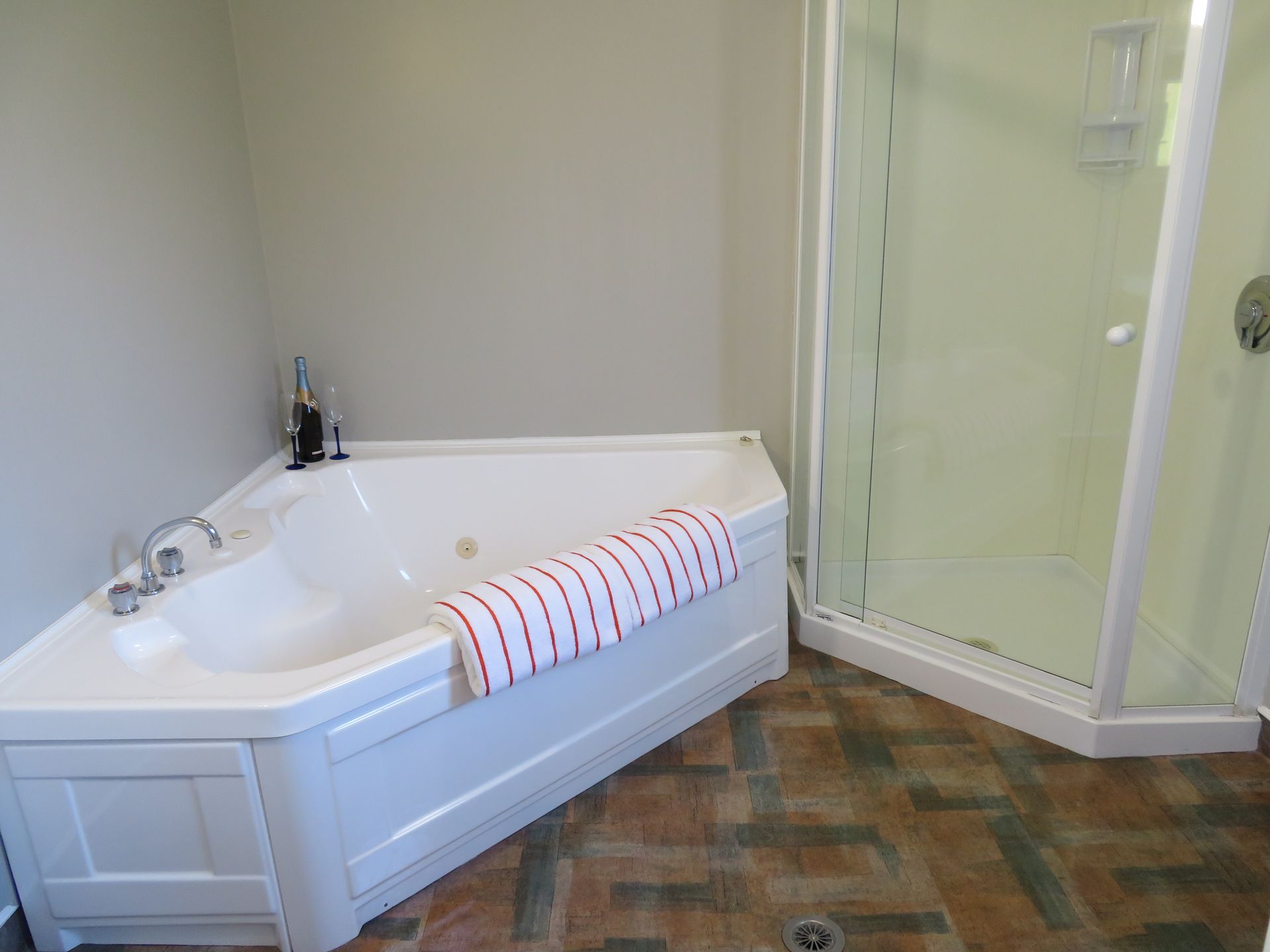 A corner jetted bathtub with a striped towel next to a glass-enclosed walk-in shower in a bathroom with tiled flooring.