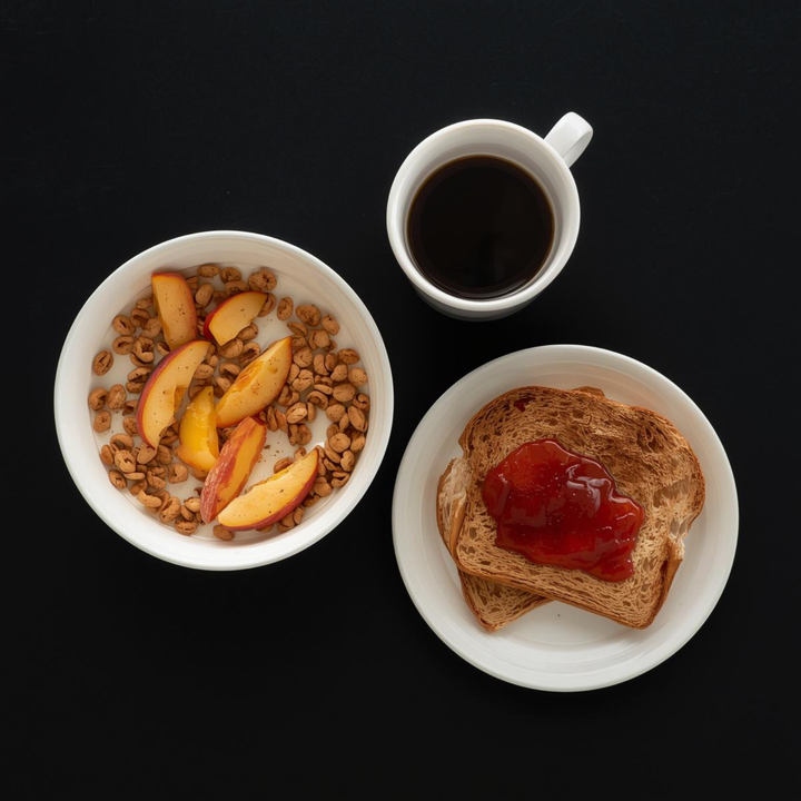 A bowl of cereal with sliced peaches, a cup of black coffee, and a slice of toast with jam on a black background.