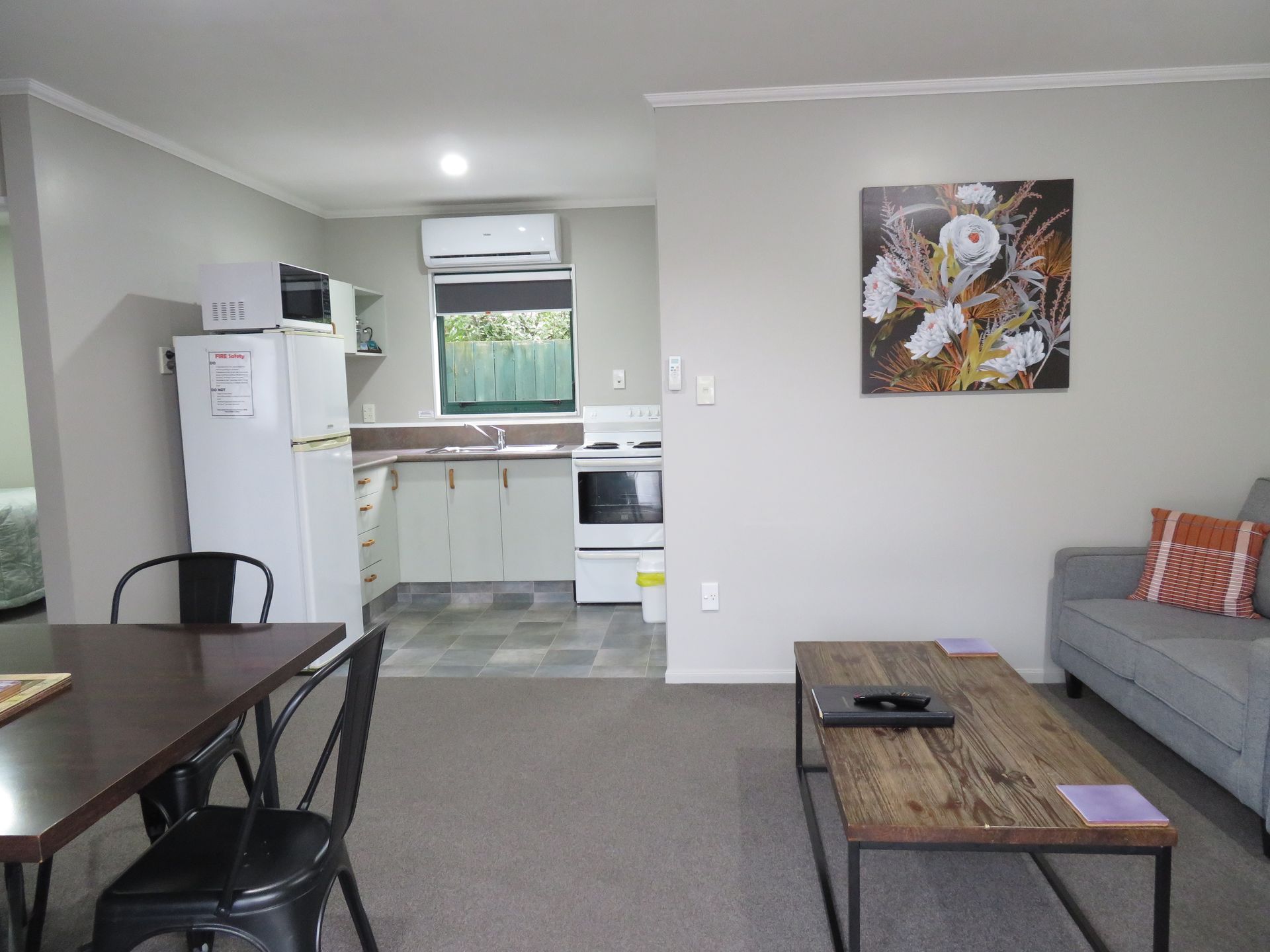 A living room flows into a kitchen with white cabinetry, a refrigerator, a dining table, and a gray sofa.