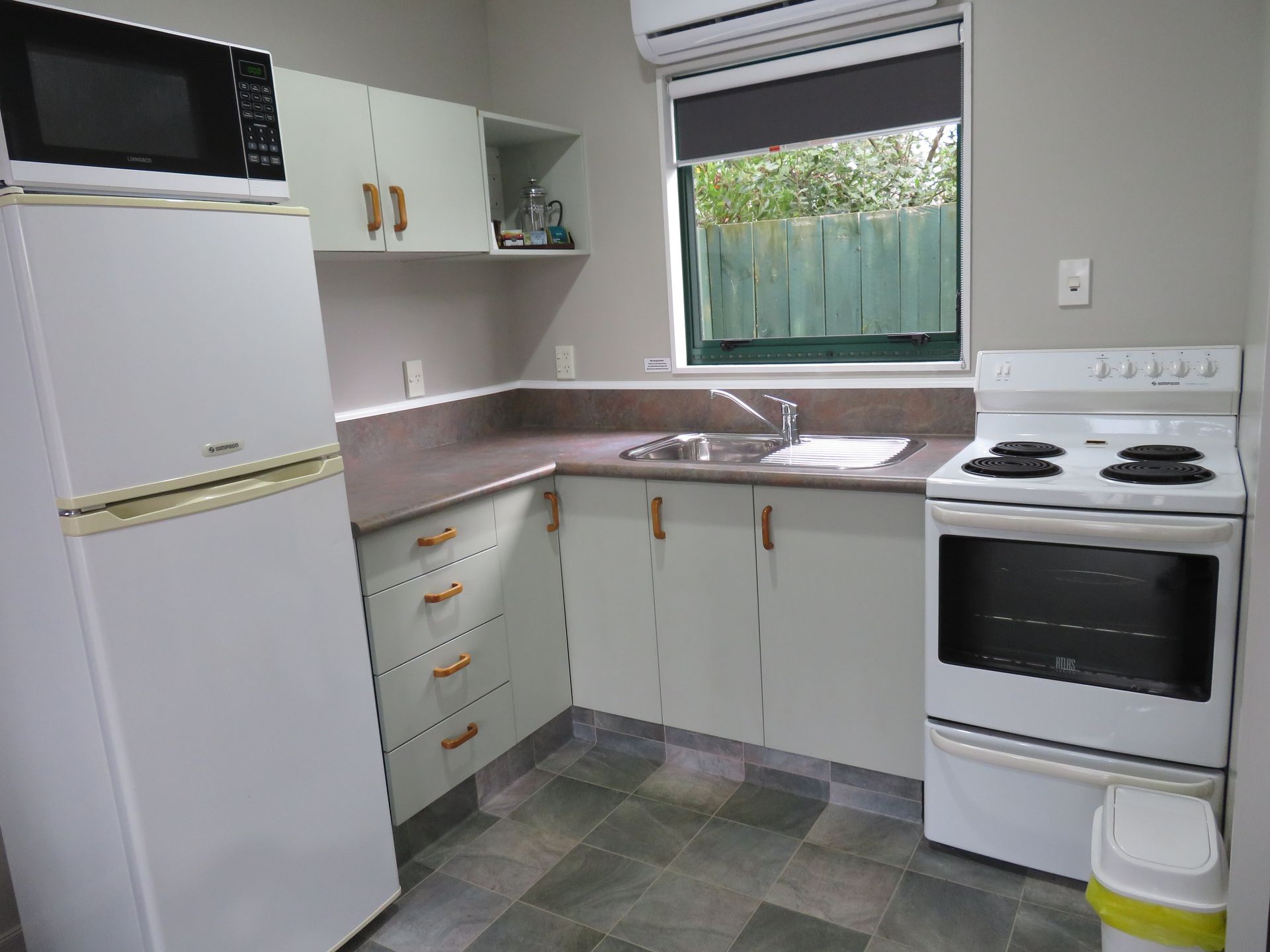 A small, U-shaped kitchen with white appliances, light-toned cabinets, dark countertops, and tile flooring.