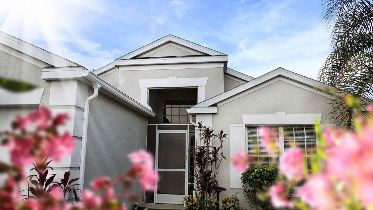 A light gray house with a screen door, framed by pink flowers. Blue sky in the background.