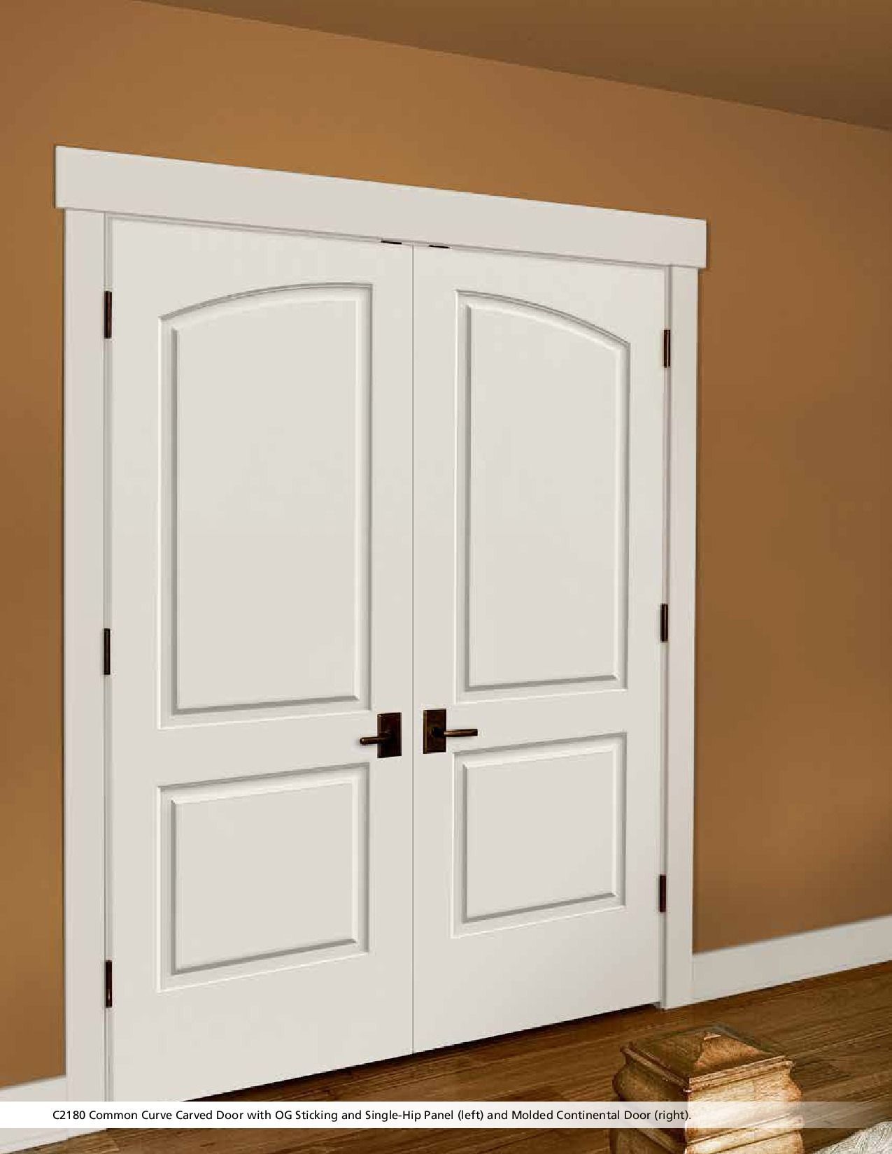 White double doors with arched top panels and dark handles in a room with brown walls.