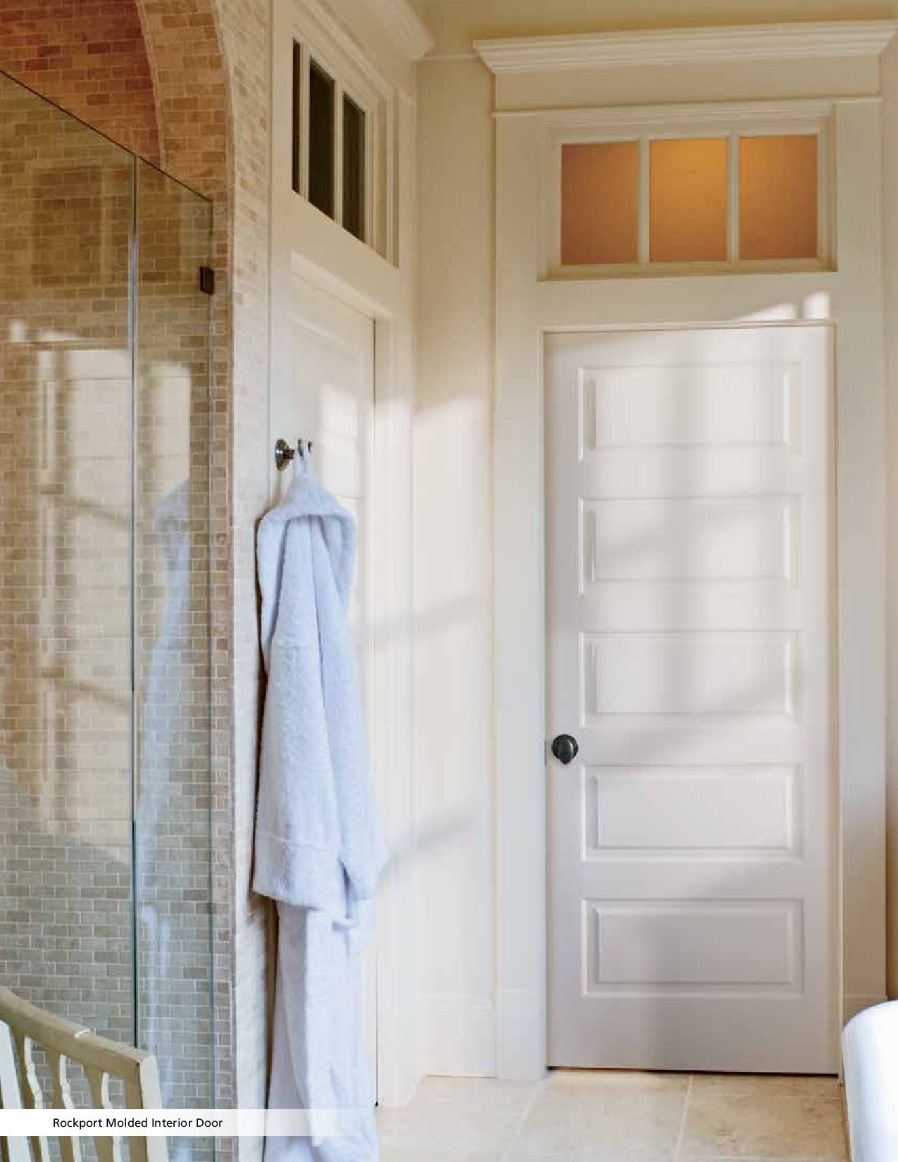 White door with black knob, robe hanging on the wall, and a shower with tiled walls.