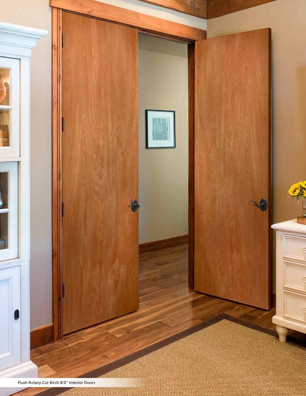 Wooden double doors open to a hallway, with a framed artwork on the wall.
