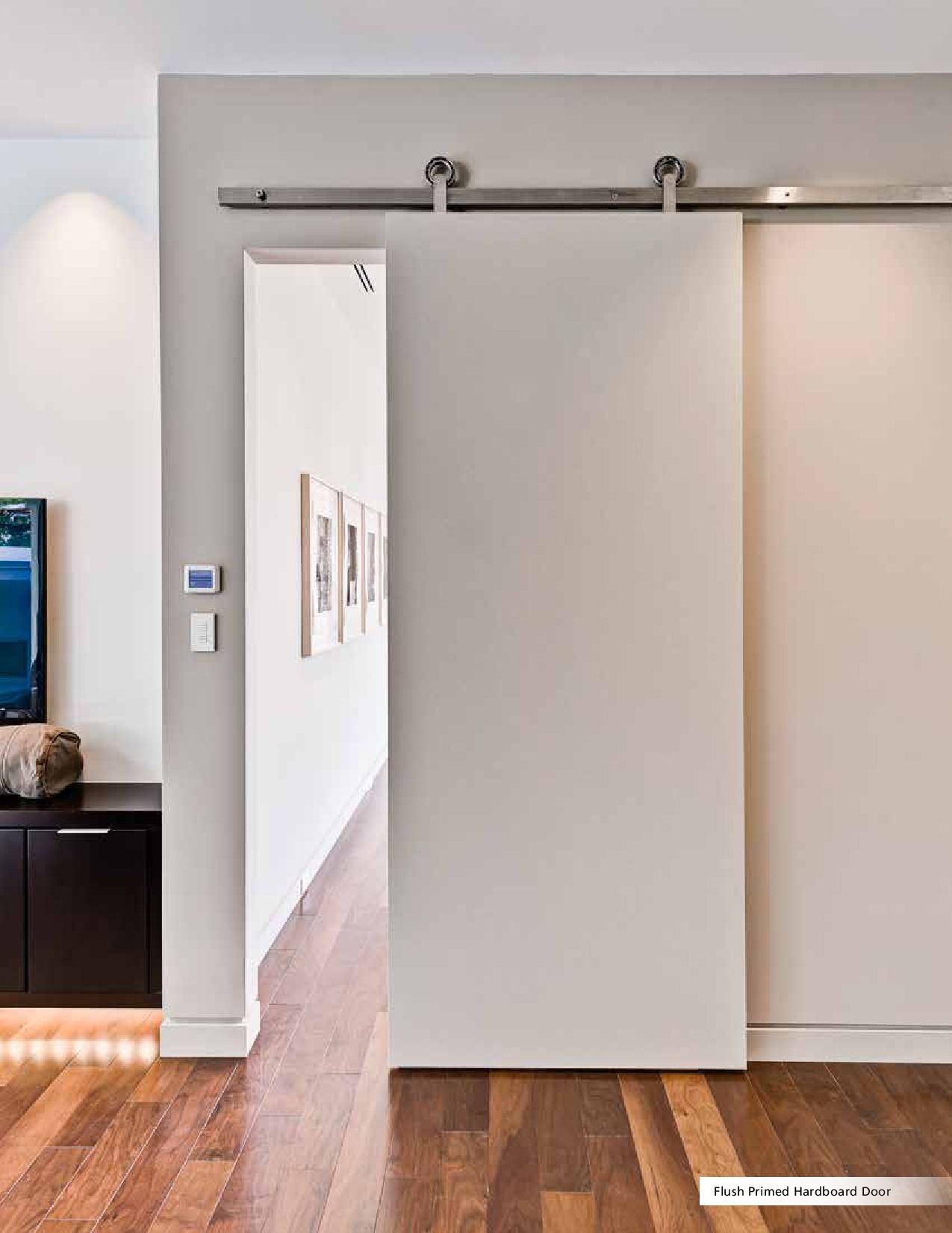 Modern sliding barn door, neutral color.  Door open, revealing hallway with framed artwork and hardwood floor.