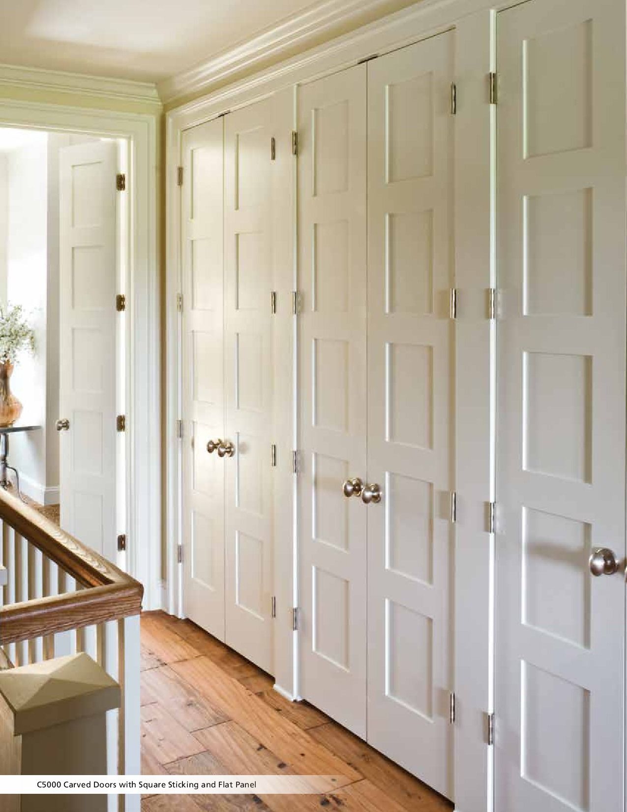 White paneled closet doors line a hallway with light wood floors and a staircase.