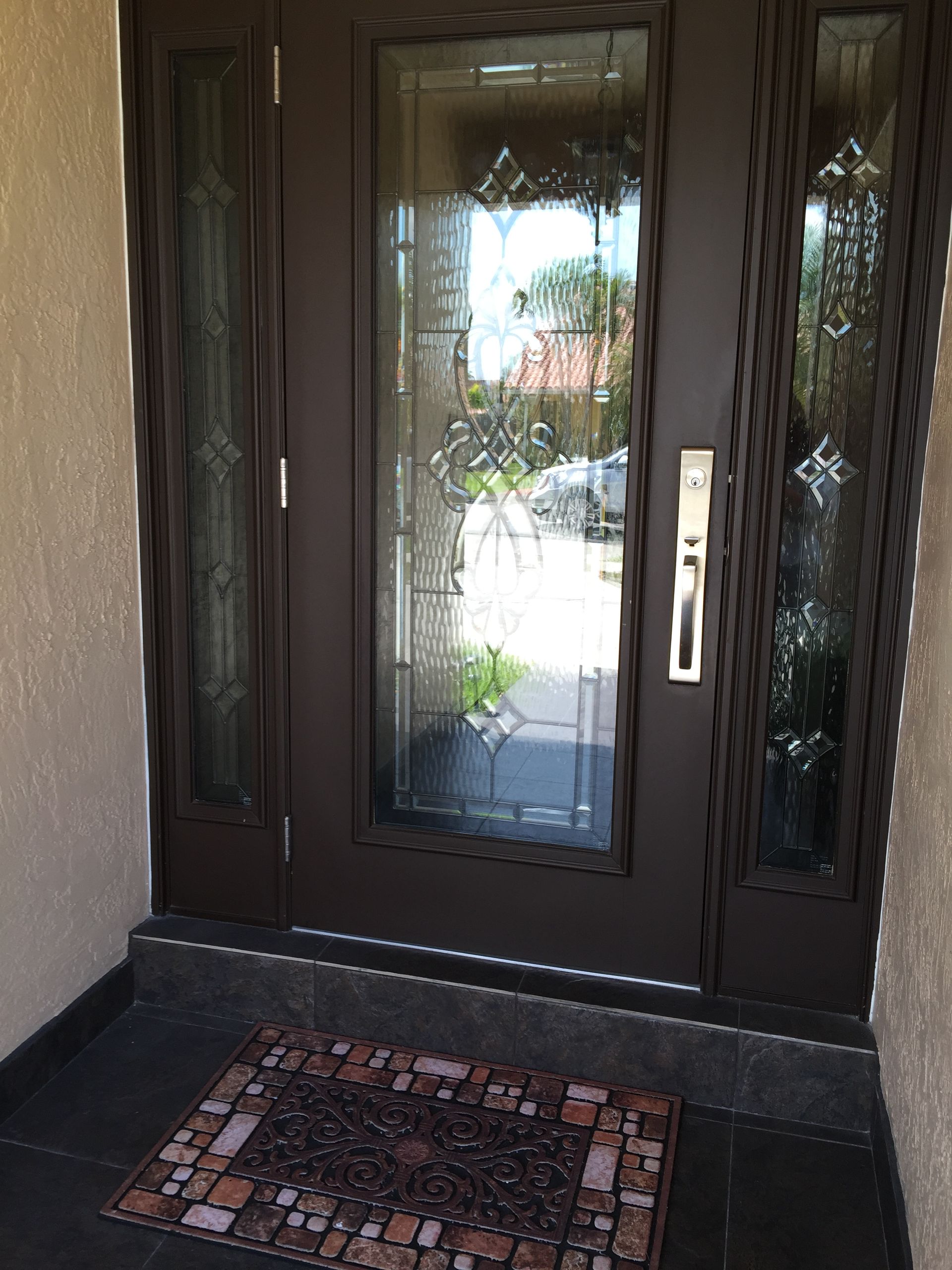 Brown front door with glass panels, doormat, and stone flooring.
