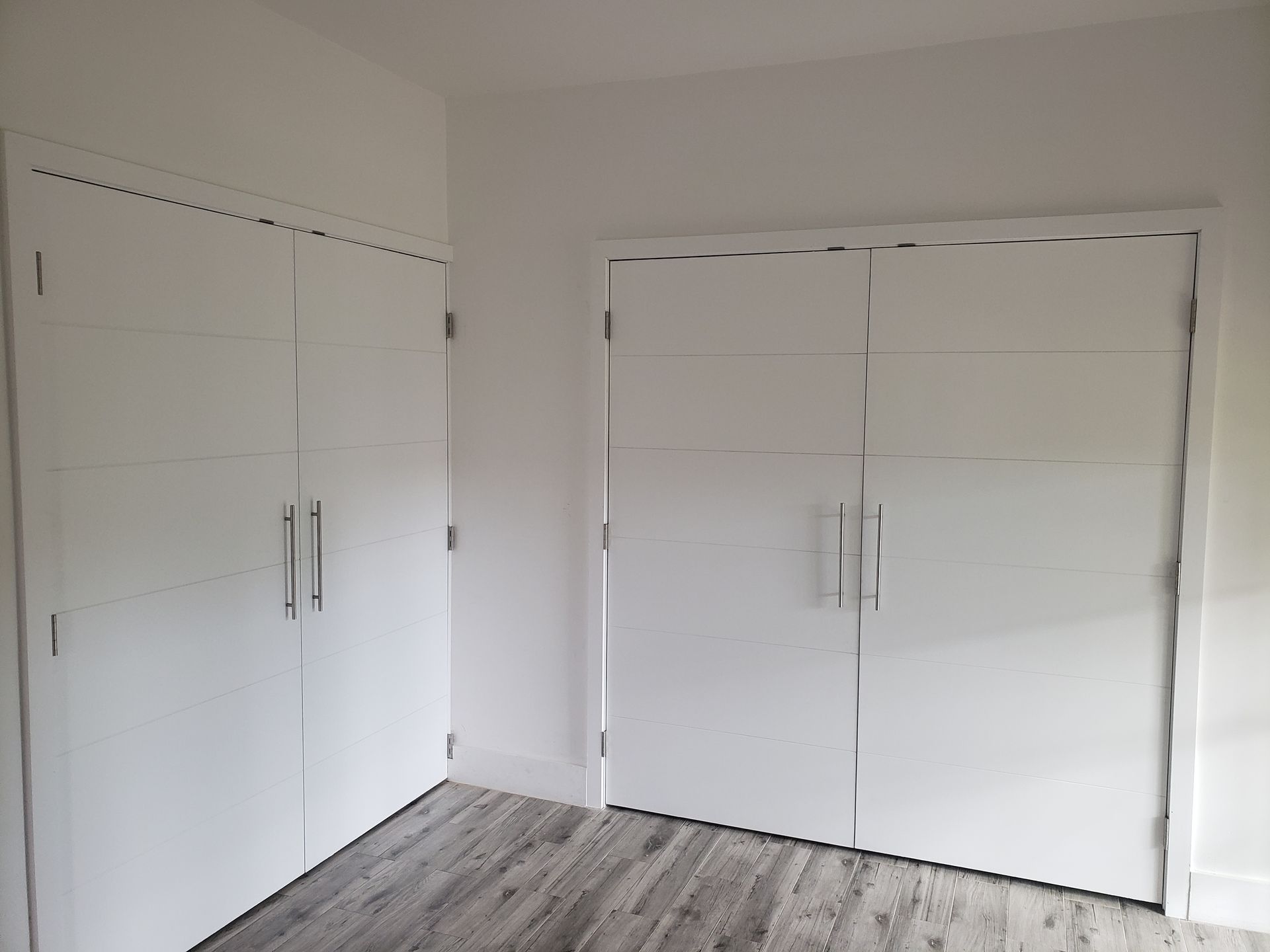 Two white, modern closet doors in a room with gray flooring and white walls.
