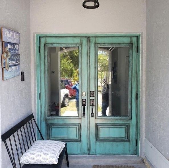 Turquoise double doors with glass panels, aged paint, open into a porch with a bench and decor.