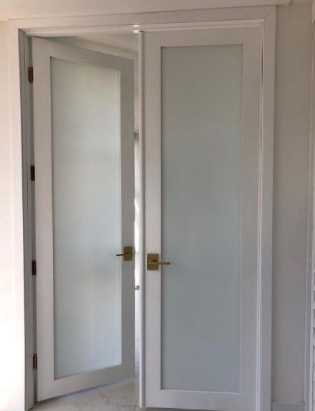 White French doors with frosted glass panels, brass handles, and white trim in a light-filled room.